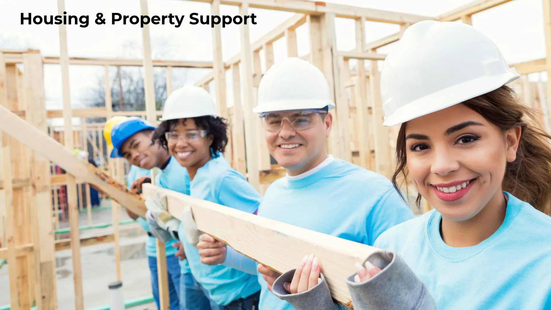 Illustrative stock photograph of construction volunteers wearing hard hats and holding lumber, with the heading Housing & Property Support; not Foundation volunteers, property or construction activities